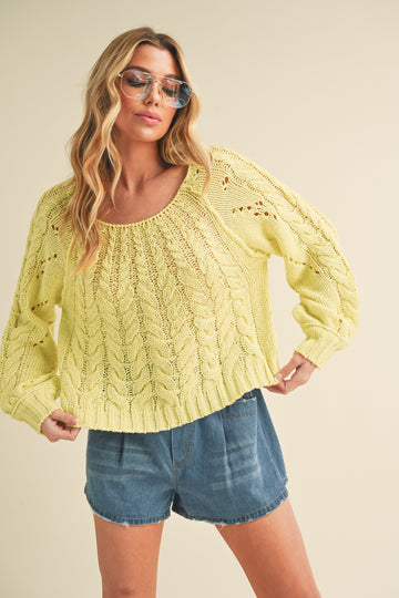woman wearing a bright yellow cable knit sweater with a scoop neckline and loose fit, paired with denim shorts