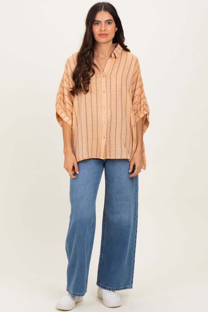woman wearing a light orange striped oversized button-up shirt with wide sleeves and blue high-waisted jeans