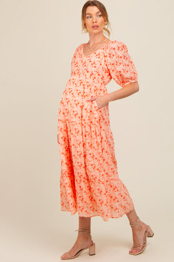 woman wearing a pink floral maternity dress with puff sleeves and pockets, highlighting her baby bump