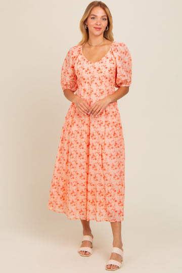 woman wearing a pink floral midi dress with puff sleeves and a v-neckline, standing and smiling