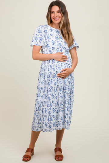 woman wearing a white floral maternity dress with short sleeves and a pleated skirt, holding her baby bump