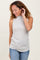 woman wearing a light gray ribbed sleeveless top and blue jeans, smiling and touching her hair