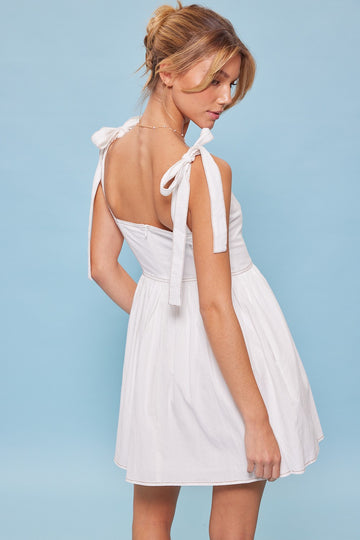 woman wearing a white sleeveless dress with bow tie straps and a flared skirt, shown from the back