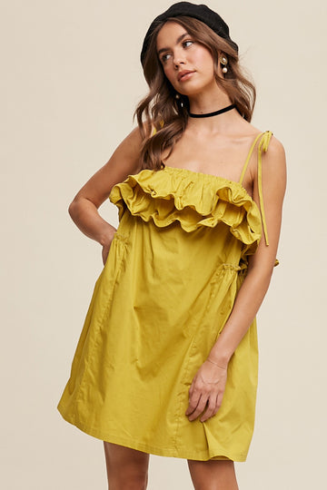 woman wearing a mustard yellow spaghetti strap ruffled sundress with a tie detail on the shoulder