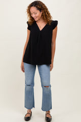 woman wearing a black ruffled sleeve top and distressed light blue flared jeans, standing and smiling