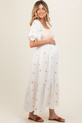 woman wearing a white maternity dress with puff sleeves and embroidered floral details, showing her baby bump