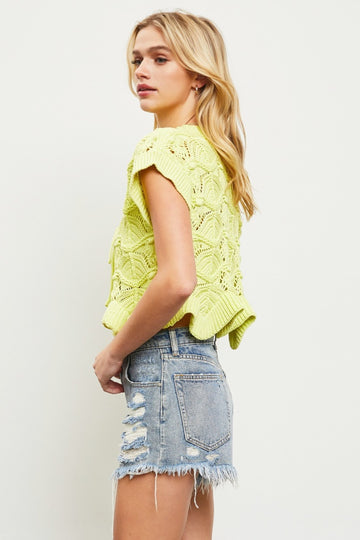 woman wearing a bright yellow knitted crop top with a scalloped hem and paired with distressed denim shorts
