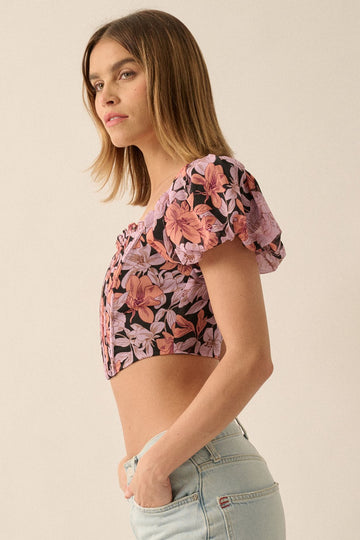 woman wearing a black floral cropped top with puff sleeves and a button-up front, paired with light blue jeans