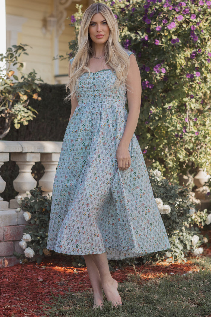 woman wearing a pastel floral print midi dress with a strapless design and flowing skirt, standing outdoors