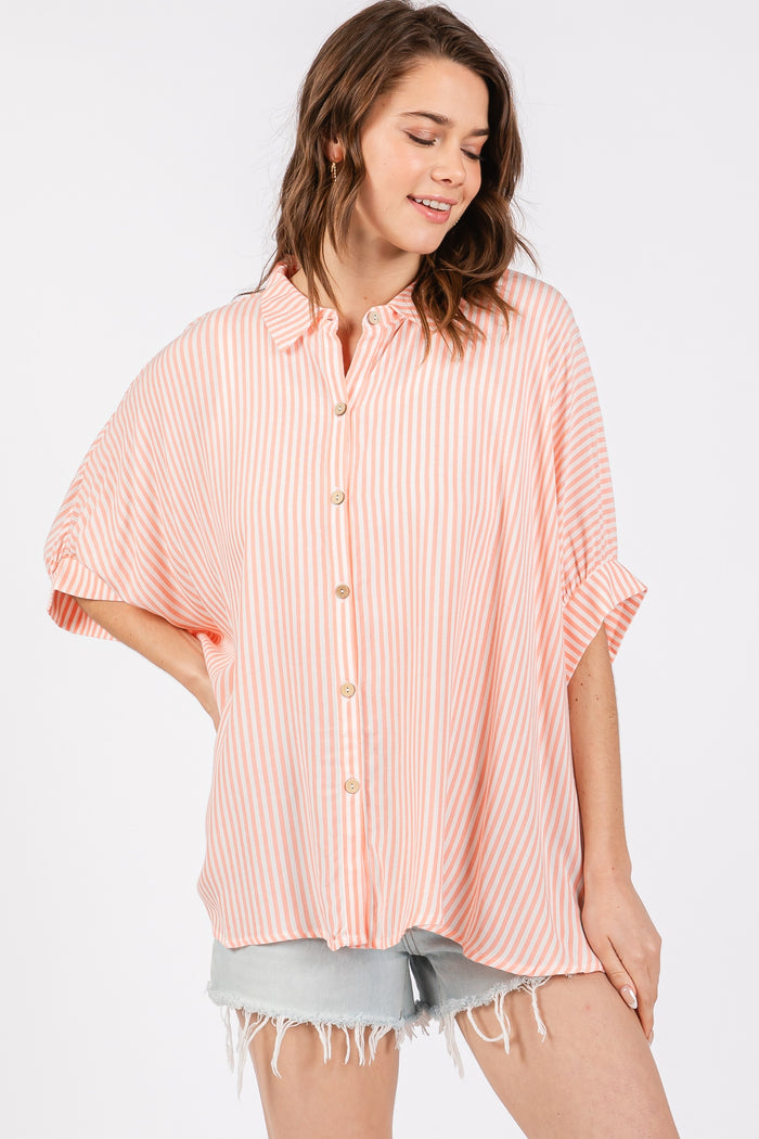 woman wearing a peach and white striped oversized button-up shirt with rolled sleeves and distressed denim shorts
