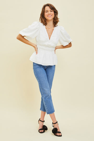 woman wearing a white puff sleeve top with a peplum waist and blue cropped jeans, styled with black heeled sandals