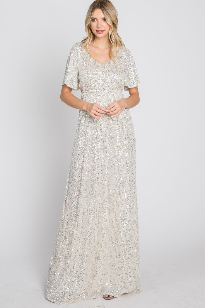 woman wearing a silver sequin maxi dress with flutter sleeves and a fitted waist