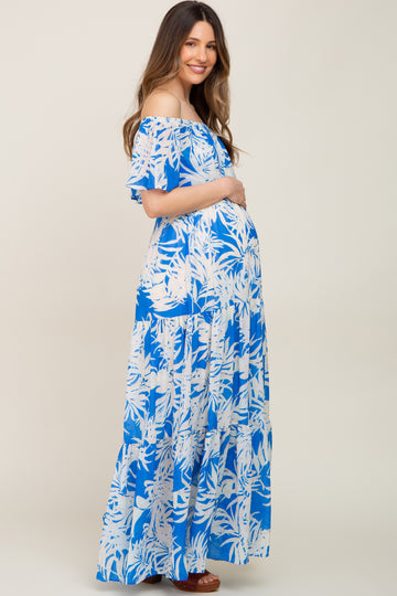 woman wearing a blue floral off-the-shoulder maternity maxi dress and holding her baby bump