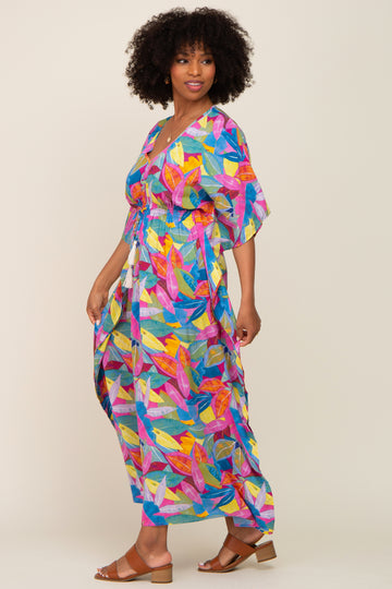 woman wearing a colorful maxi dress with leaf patterns and a drawstring waist, standing with a smile