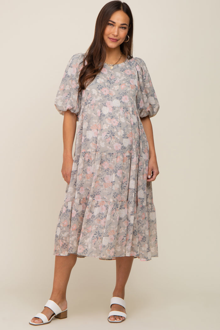 Woman wearing a grey floral tiered midi dress with puff sleeves and white sandals