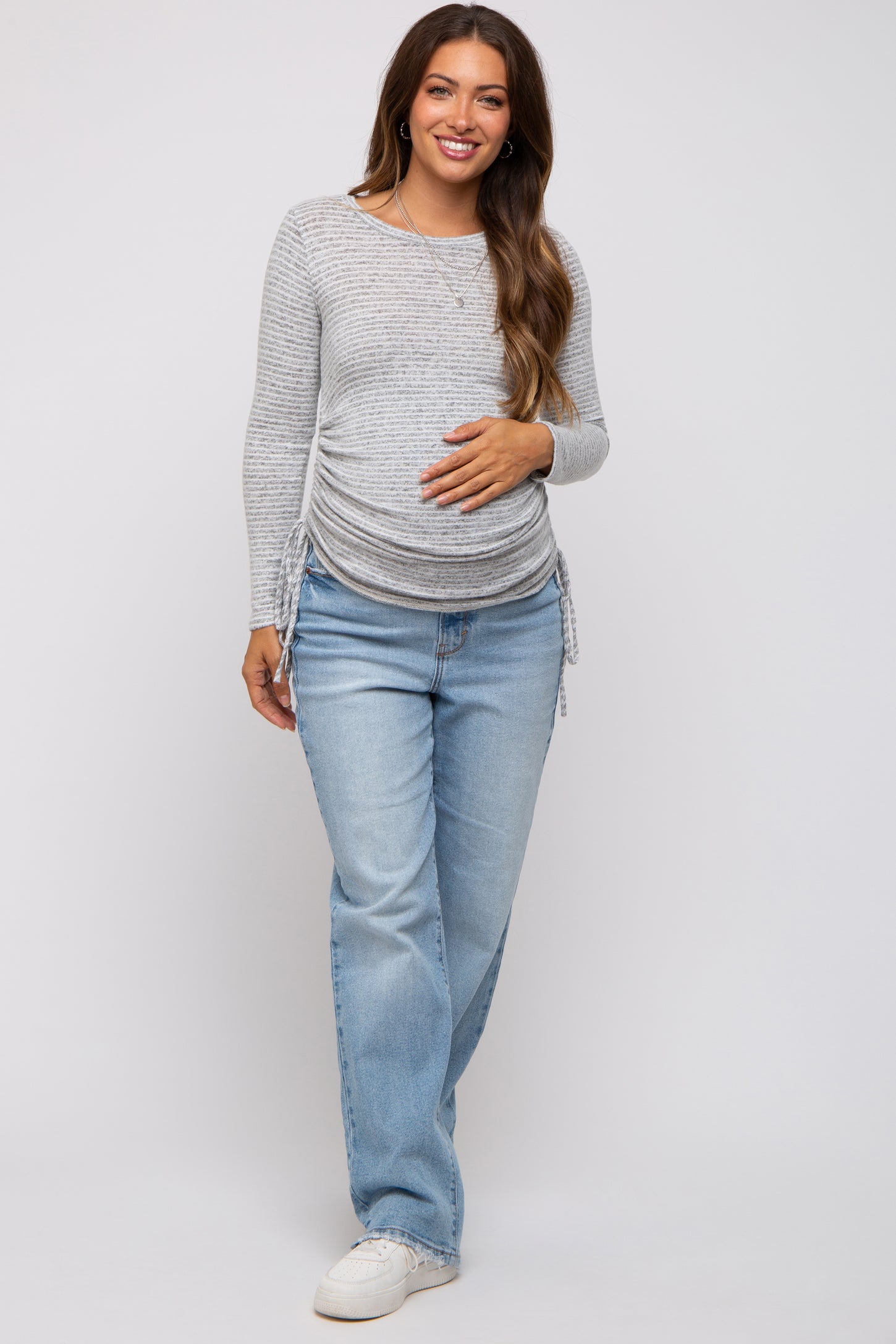 woman wearing a light gray striped long sleeve maternity top with side ruching and blue jeans, showcasing her baby bump