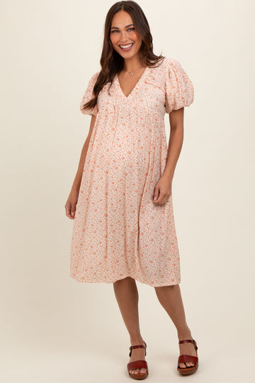 woman wearing a peach floral maternity dress with puff sleeves and a v-neck, showing her baby bump