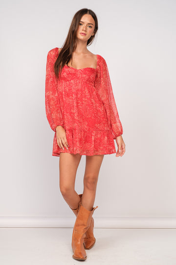 woman wearing a red floral long sleeve mini dress with a ruffled hem and tan ankle boots