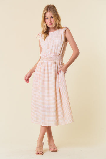 woman wearing a light pink gingham midi dress with tie shoulder straps and pockets